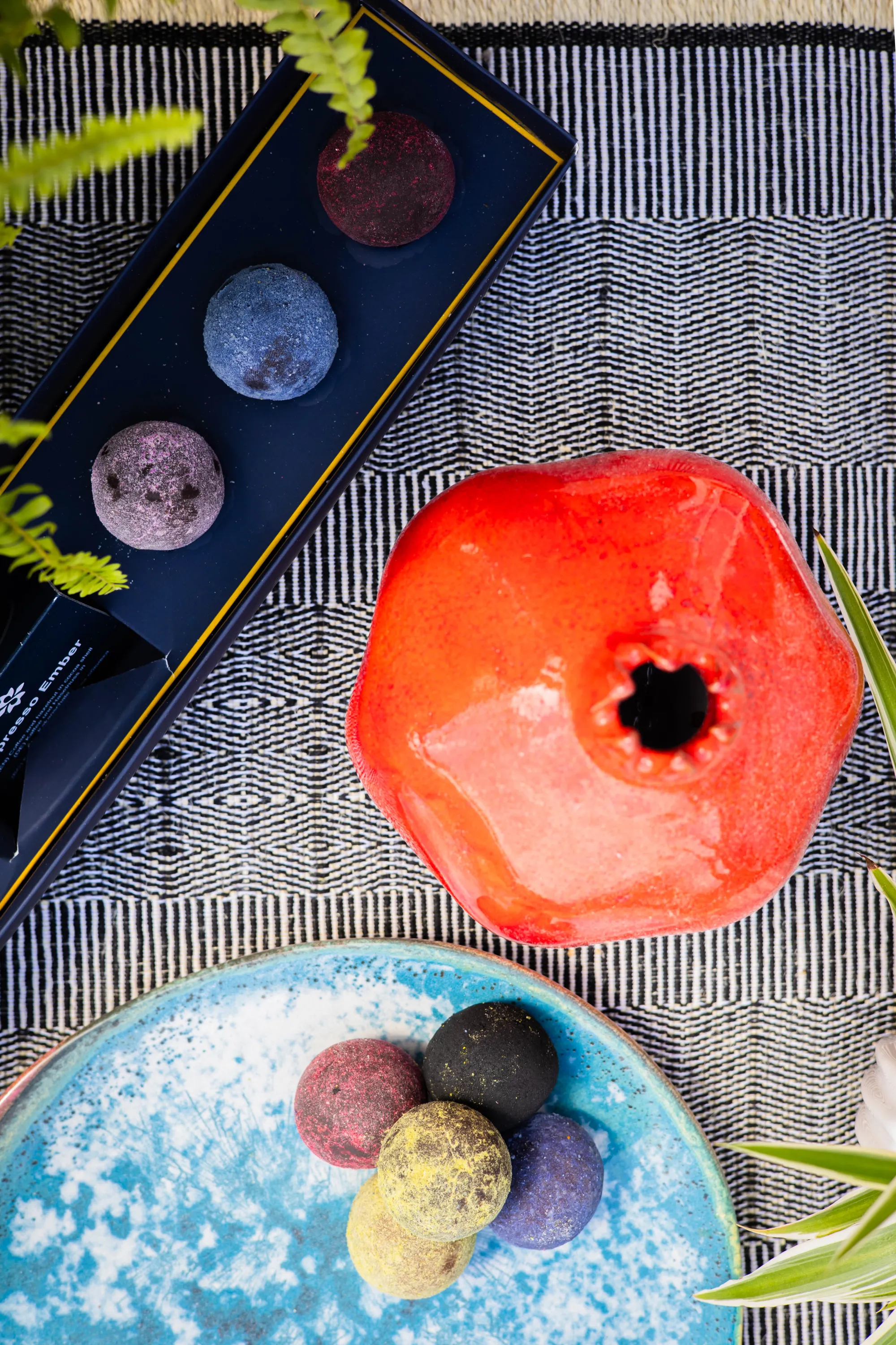 One open box of Senarro bliss balls, next to an artsy red vase, with a plate of arranged Senarro bliss balls below